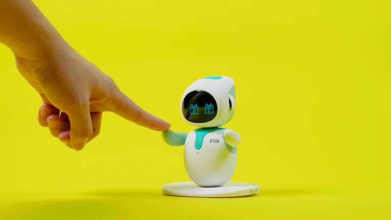 Eilik robot by Energize Lab interacting with a human hand against a yellow background.